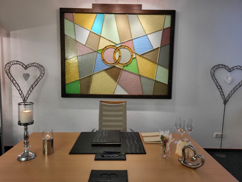 Trautisch Rathaus Trautisch mit Stühlen, Ringablage, Sektgläsern und einem buntem Wandbild auf denen zwei Ringe zu sehen sind