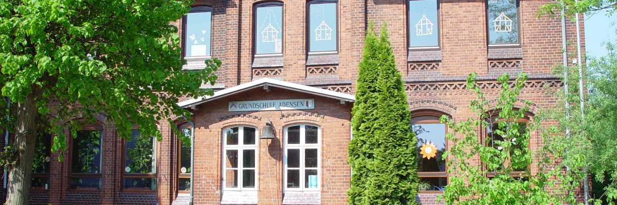 Grundschule Adensen rotes Backsteinhaus umrahmt von grünen Bäumen