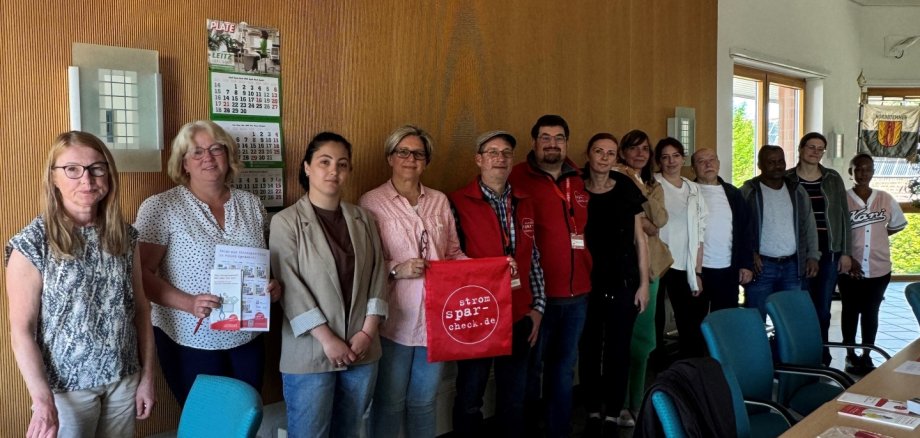 Eine Gruppe von Menschen zeigt Informationsmaterial zum Stromspar-Check im Sitzungssaal des Rathauses.