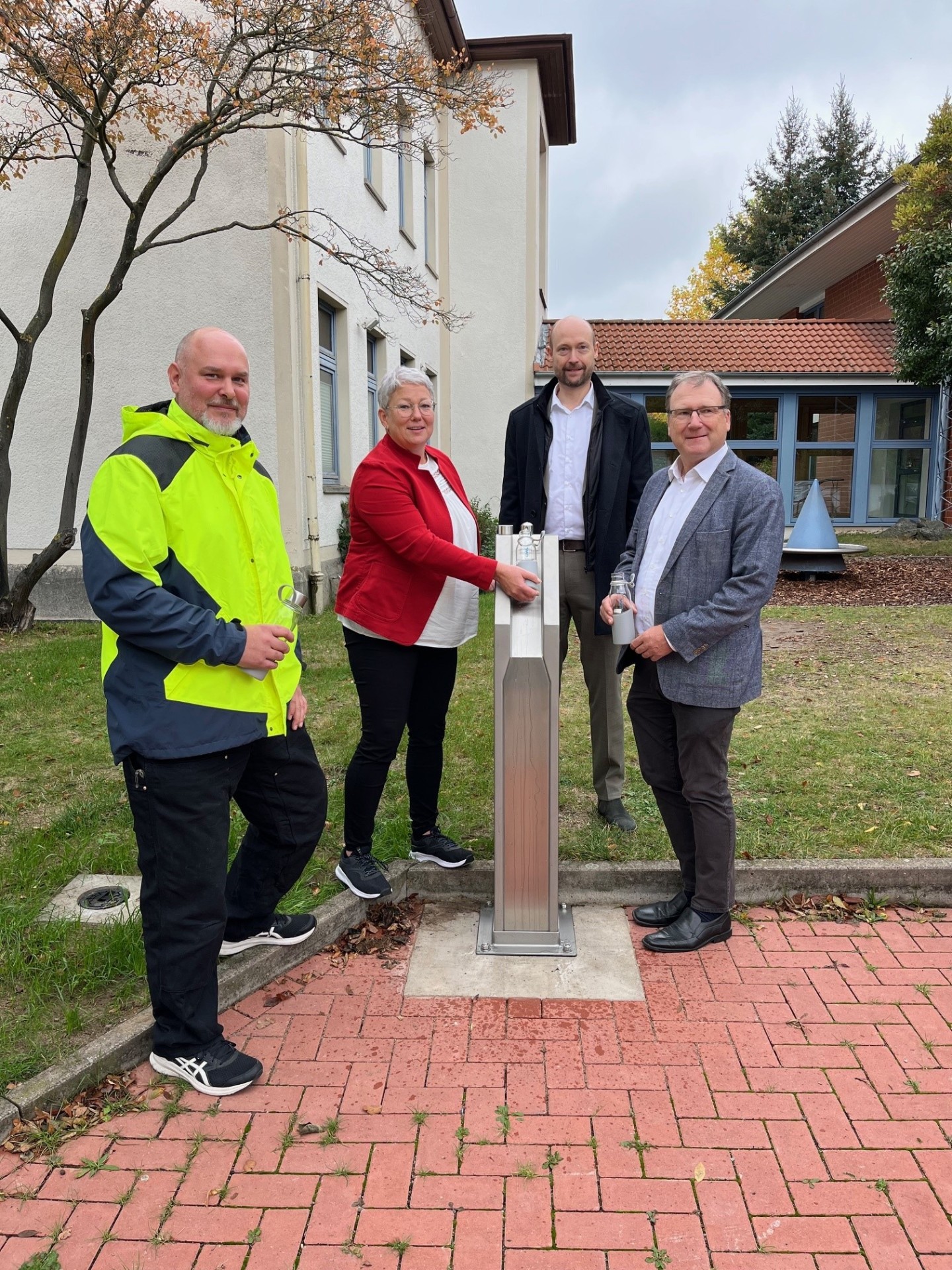 Einweihung des Trinkwasserbrunnens: Vier Personen stehen am Brunnen am Rathaus. Es wird Wasser aus dem neuen Wasserspender gezapft.