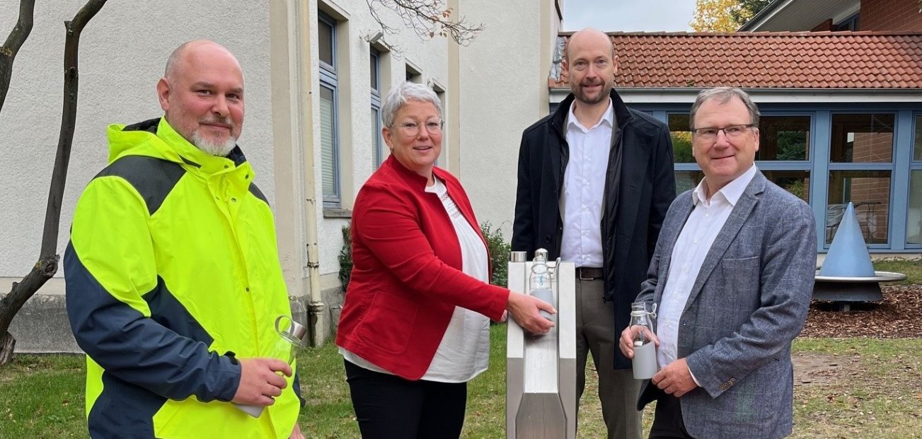 Einweihung des Trinkwasserbrunnens: Vier Personen stehen am Brunnen am Rathaus. Es wird Wasser aus dem neuen Wasserspender gezapft.