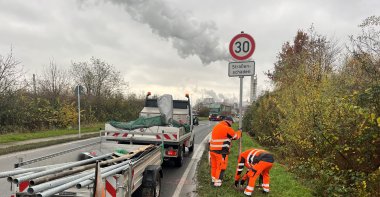Zwei Bauhofmitarbeiter mit Verkehrsschild 30 am Straßenrand mit Fahrzeug