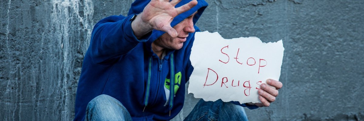 Drogen sitzende Person  mit Schild "Stop Drugs"